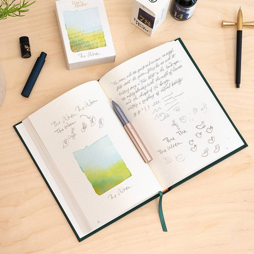 Open notebook with writing and watercolor illustrations on a wooden surface, surrounded by stationery items.